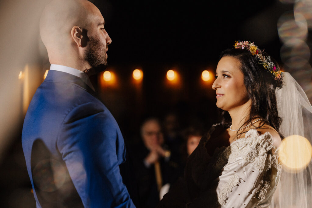 Couple exchanging vows at an intimate evening micro wedding ceremony, warm bokeh lights in the background, documentary wedding photography by Honey & Bloom