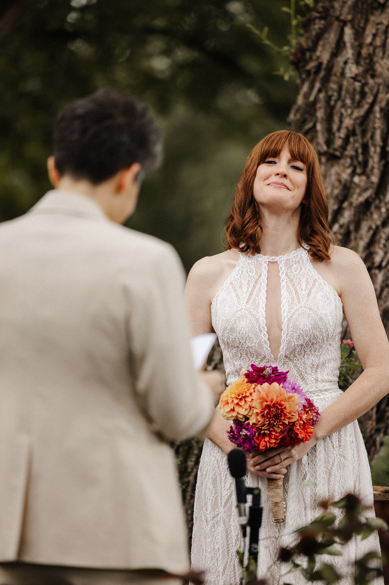 Bride smiling during outdoor micro wedding vows, holding a colorful dahlia bouquet, intimate ceremony photographed by Honey & Bloom Photography in Central New York