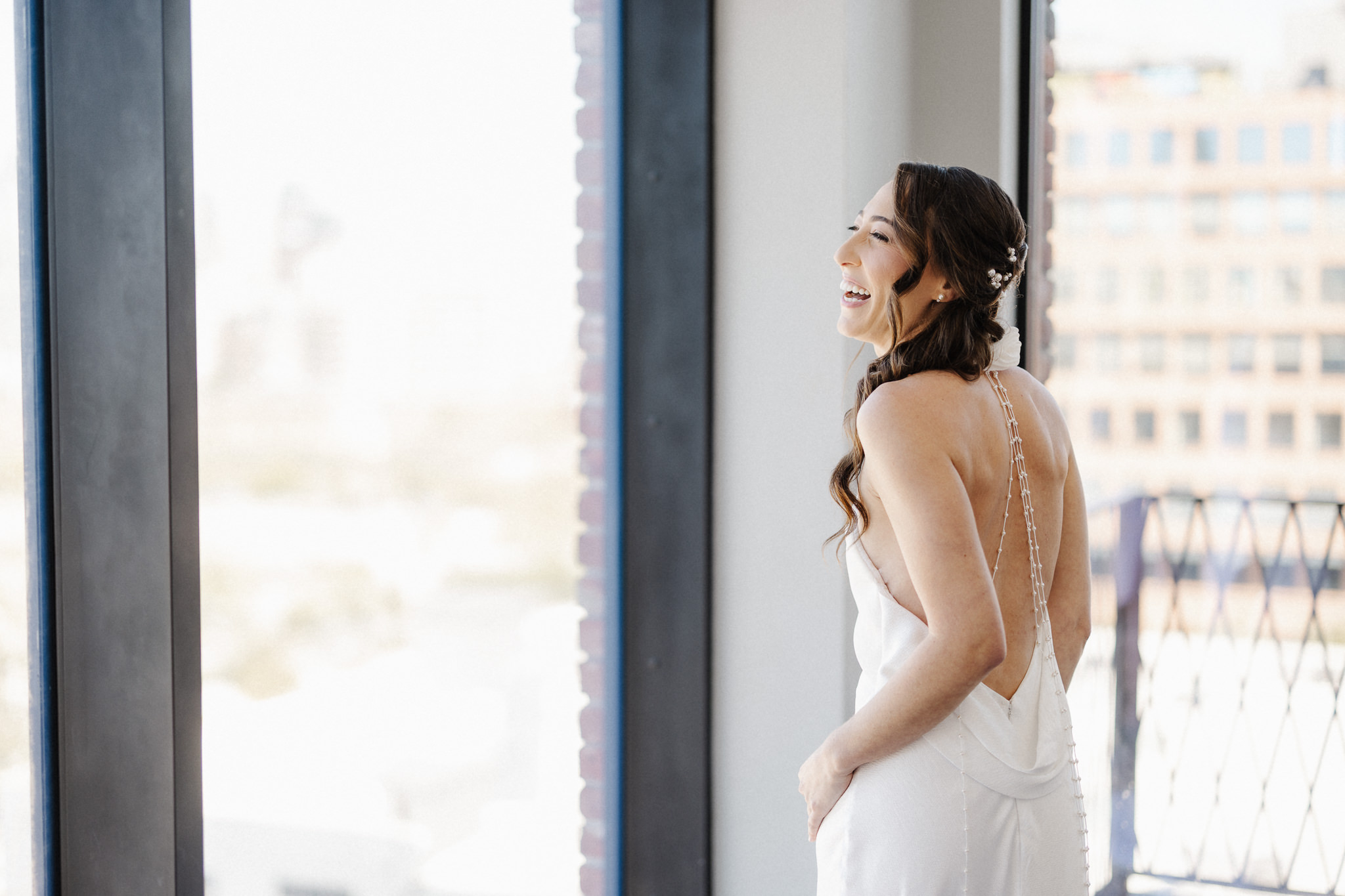 Bride laughing at a window on her wedding morning, a spontaneous unplanned moment