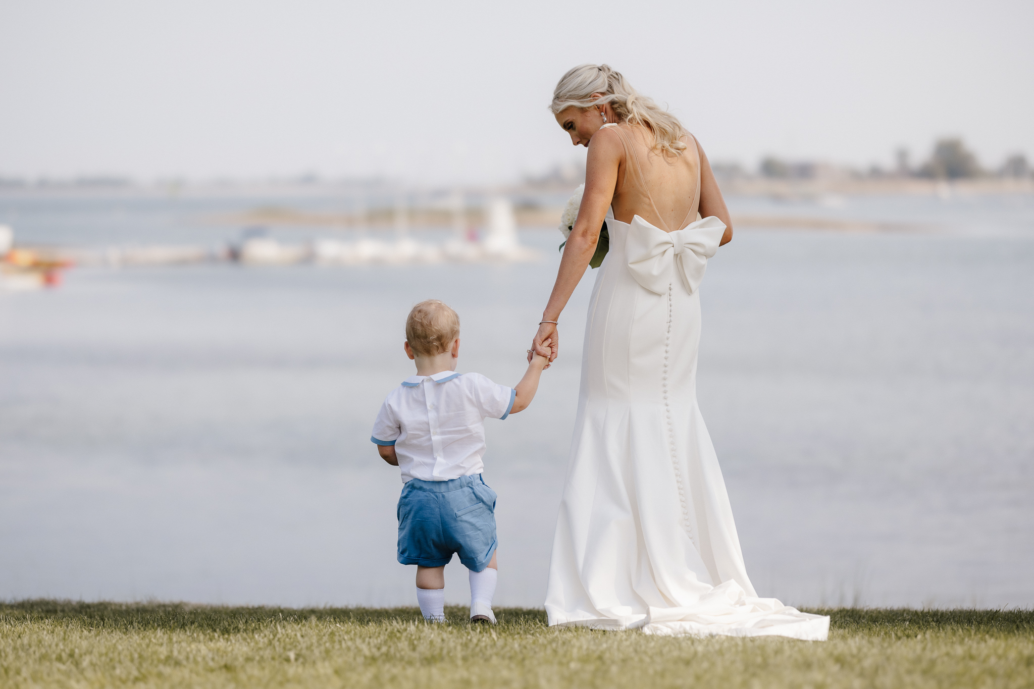 Bride holding a small child’s hand at a waterfront wedding, documentary wedding photography by Honey and Bloom