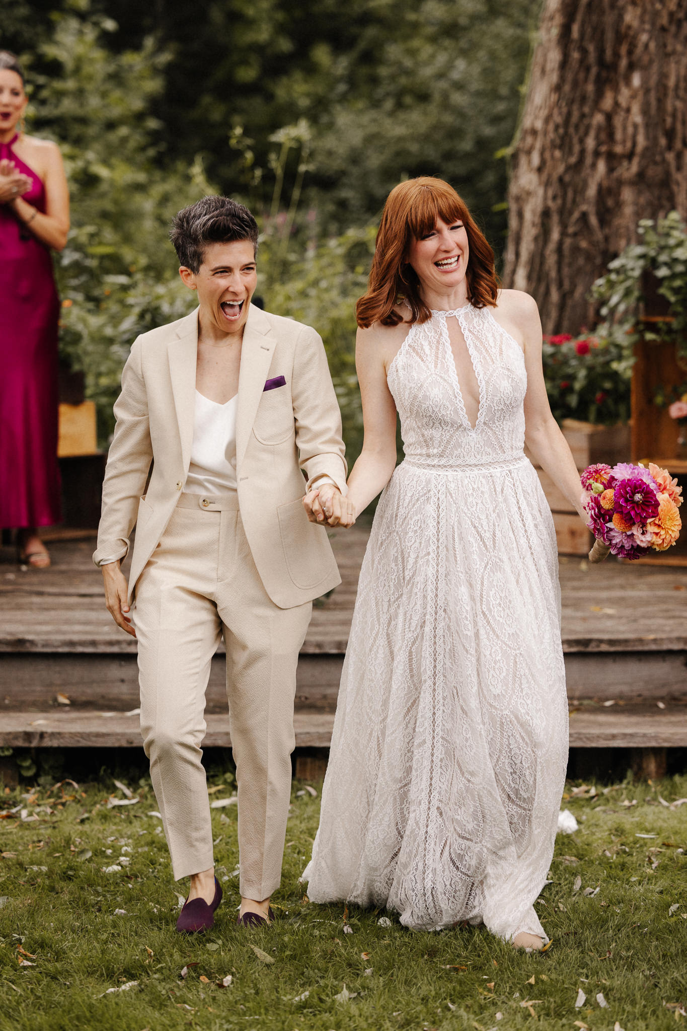 Two newlyweds laughing and holding hands after their outdoor wedding ceremony.