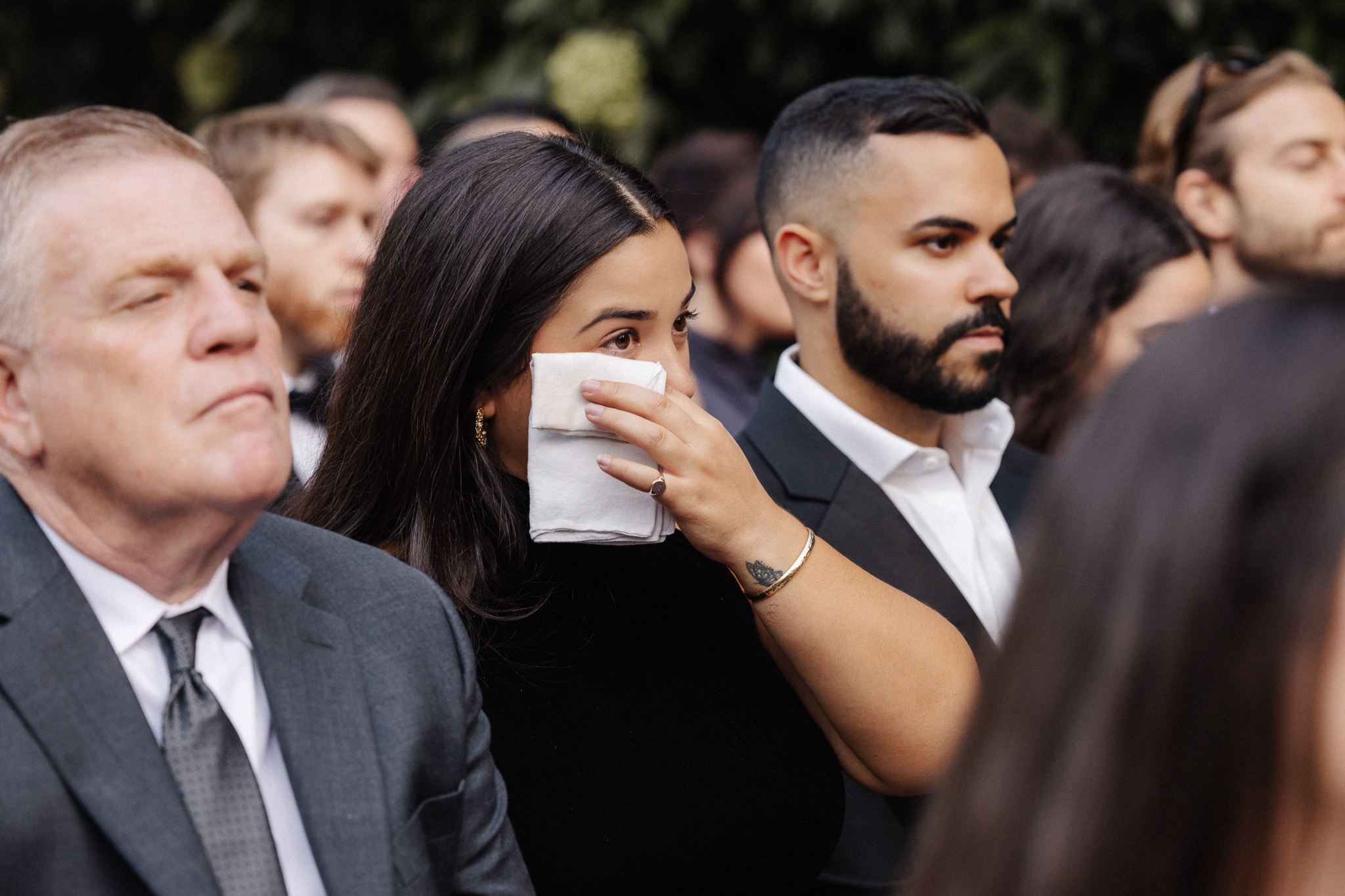 Wedding guest wiping away tears during an outdoor ceremony.